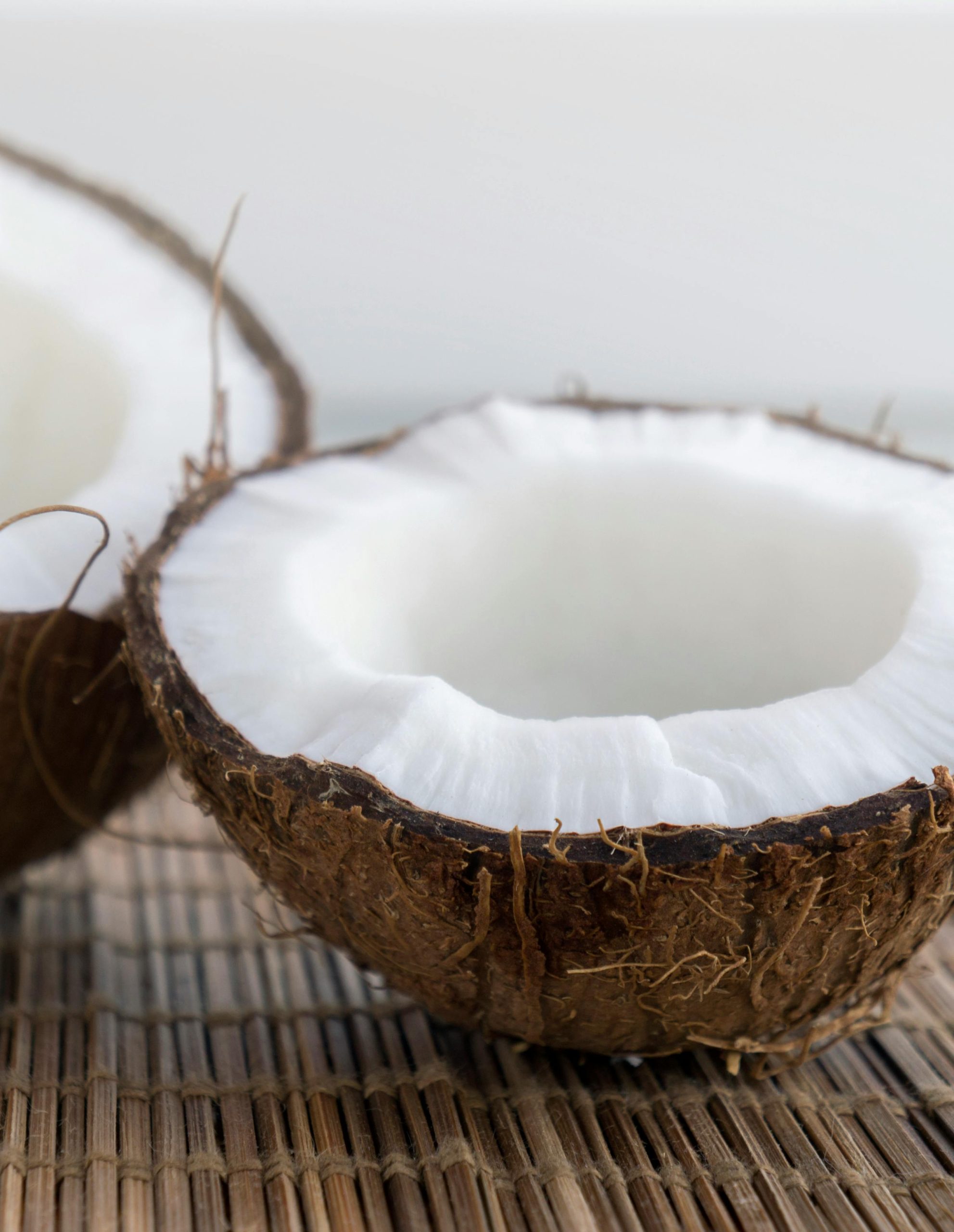 Vertical shot of fresh coconut halves on a rustic woven mat, showcasing white interior against a natural backdrop.